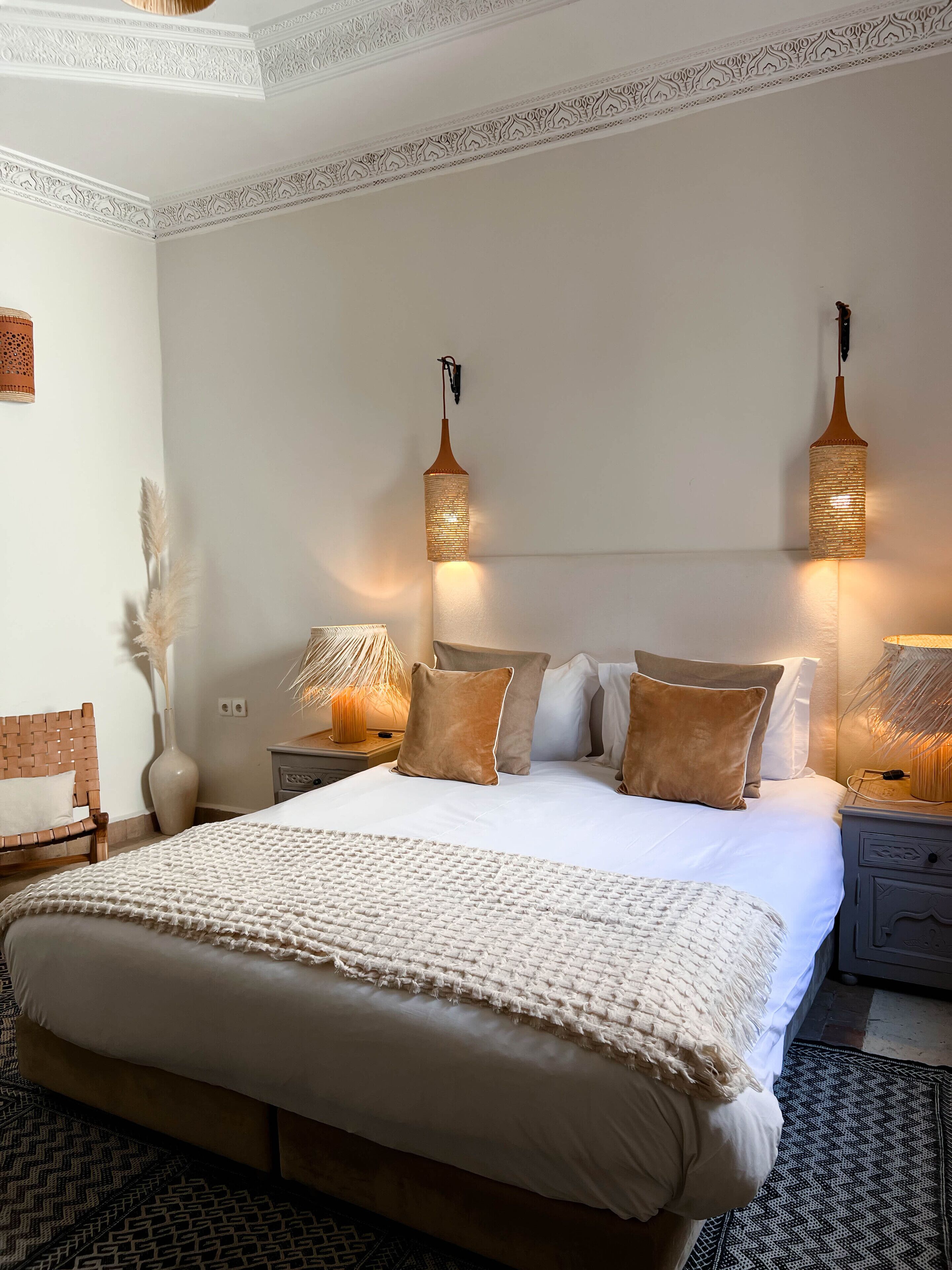 Un dormitorio ordenado con una cama grande, dos lámparas de noche y un jarrón decorativo.