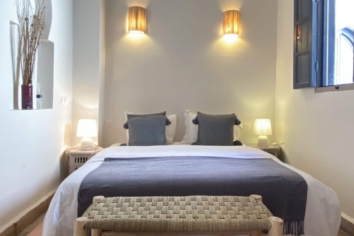 A bedroom with a large bed, two bedside lamps, a bench, and a patterned rug.