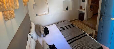 A bedroom with a bed, bedside lamps, a hanging light fixture, a mirror, and a door leading to another room.