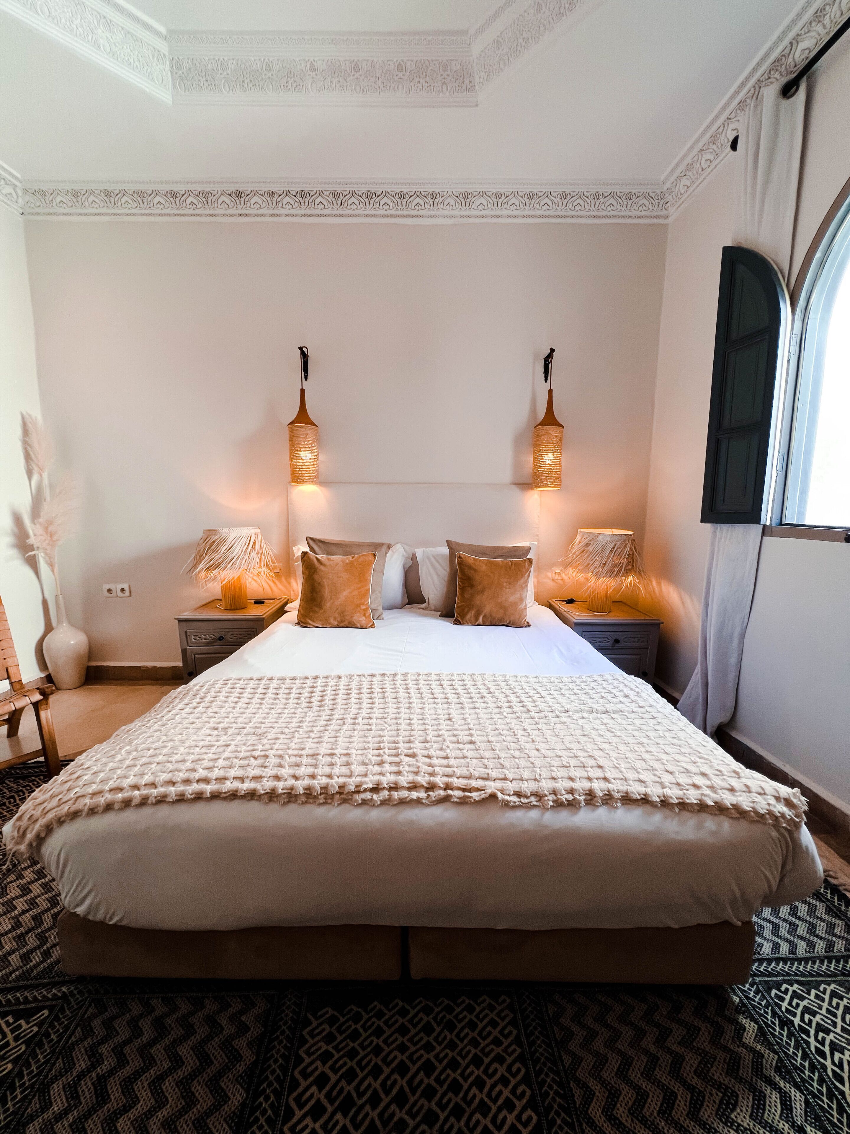 A large bed with a patterned bedspread, two bedside lamps, and a decorative vase on the nightstand.