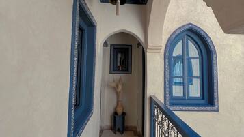Un pasillo con puertas de marco azul, una campana colgante y un jarrón decorativo con plumas de pámpano.
