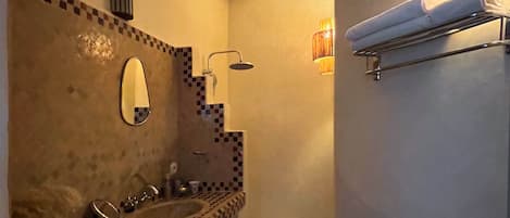 A bathroom with a checkered tile backsplash, a sink, a mirror, a towel rack, and a shower with a wall-mounted light.