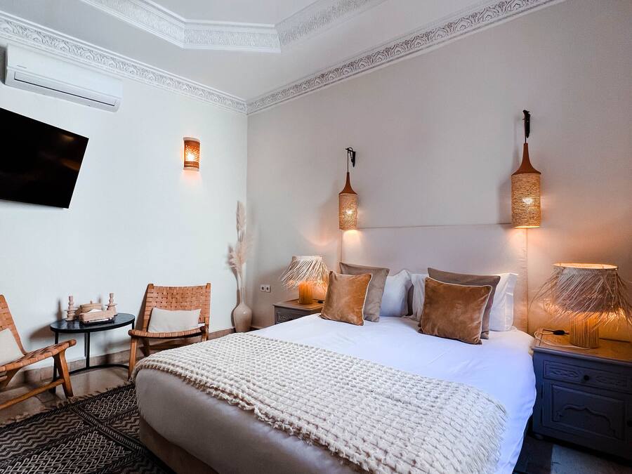 Quarto de hotel com uma cama grande, duas mesas de cabeceira, uma televisão e uma luminária decorativa no teto.