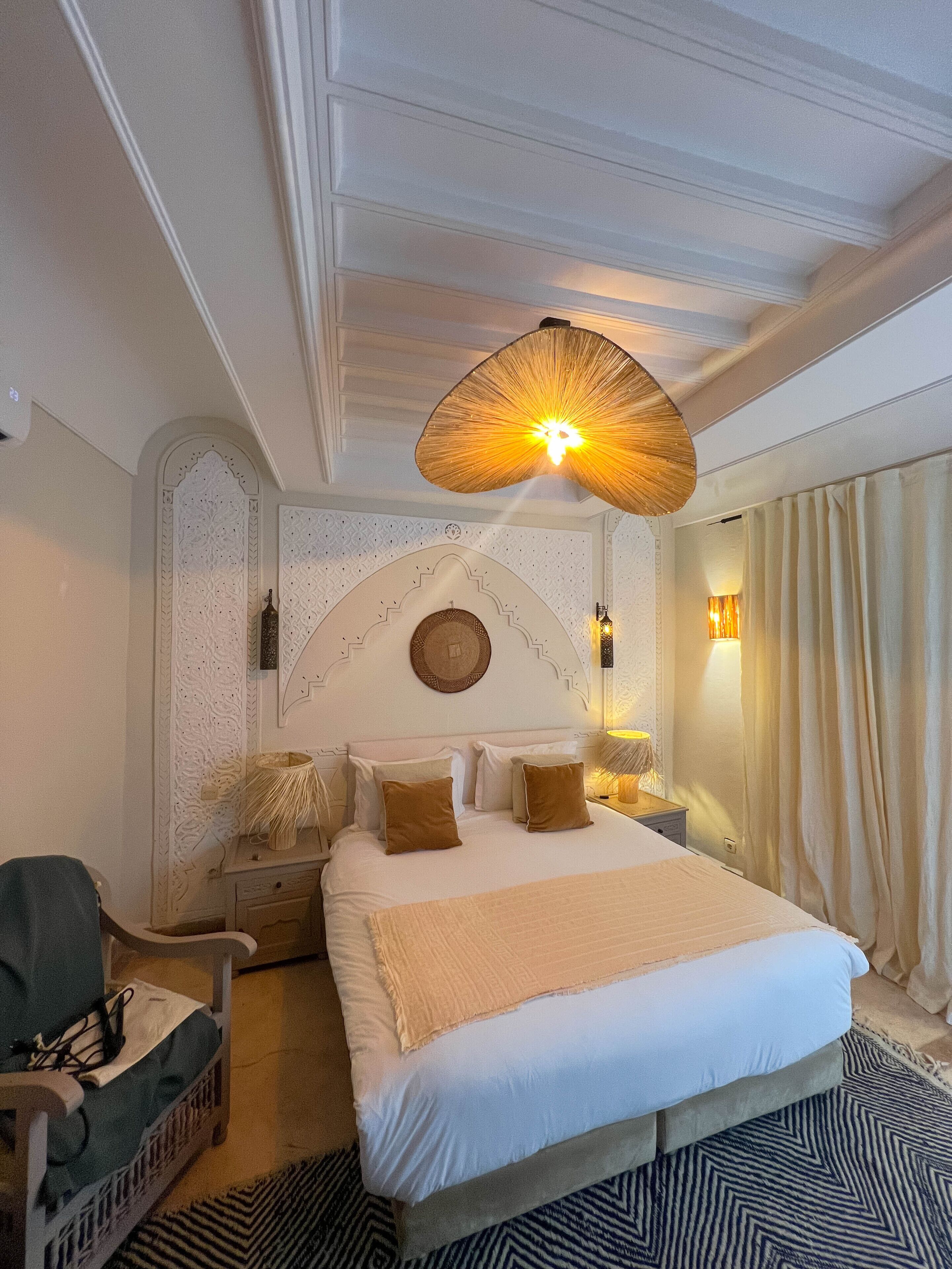 A hotel room with a large bed, a chair, a nightstand, and a wall-mounted lamp.