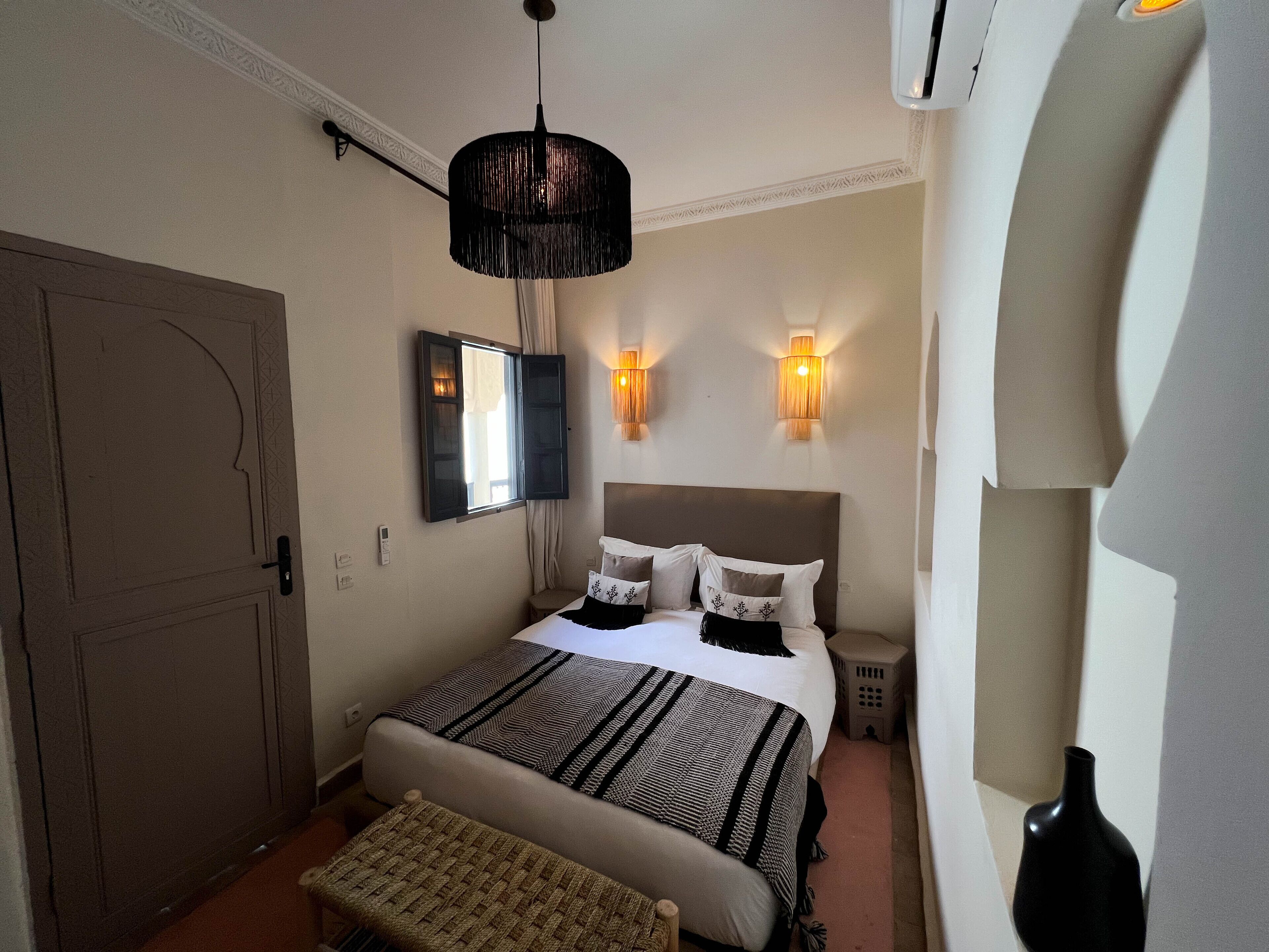 A bedroom with a bed, bedside tables, a hanging light fixture, and a wall-mounted lamp.