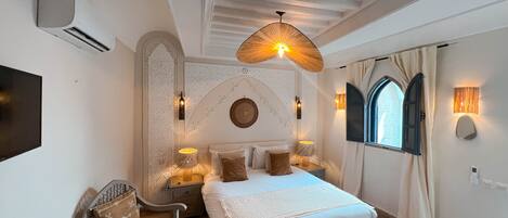 A bedroom with a bed, bedside lamps, a chair, a television, and a window with curtains.