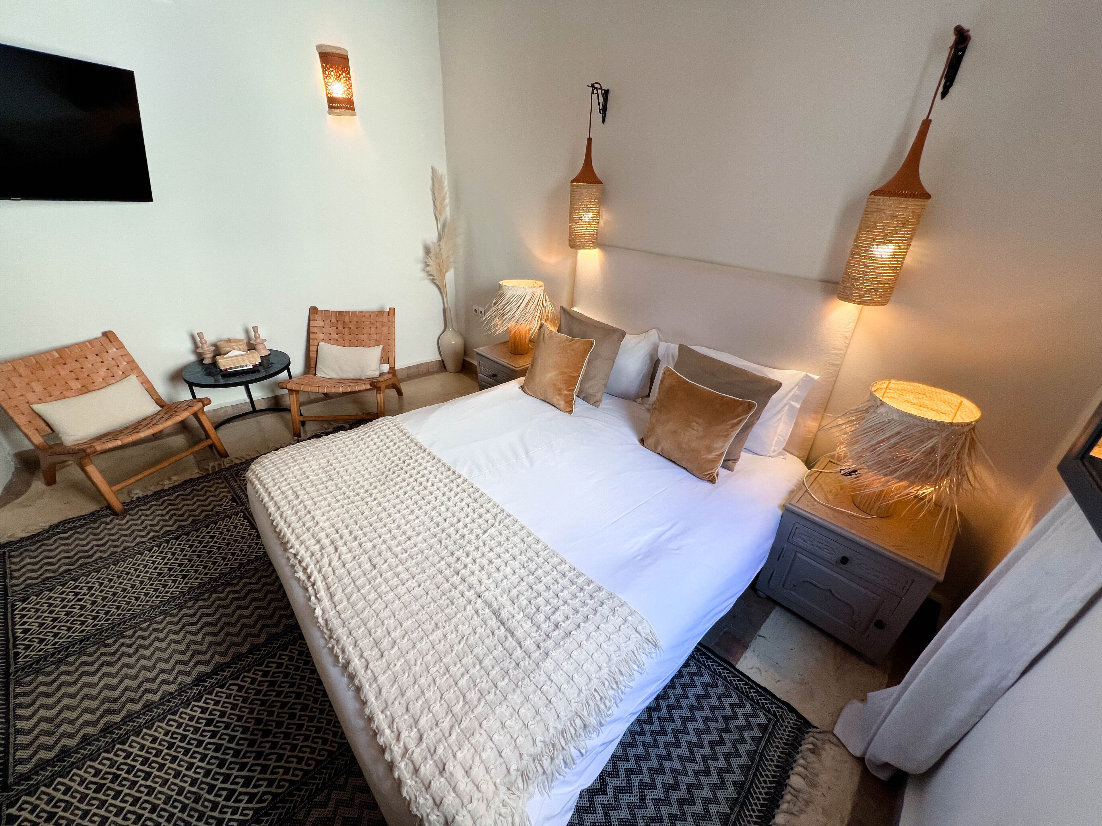 A neatly arranged bedroom with a large bed, two bedside tables, a chair, and decorative wall lights.