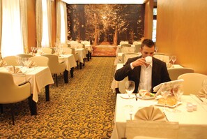 A formal dining room with tables set for a meal, featuring a carpeted floor and a forest-themed wall mural. - Hotel Hercegovina (Sarajevo)