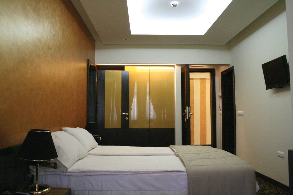 A hotel room with a bed, a nightstand, a lamp, a TV, and a wardrobe with a mirror.