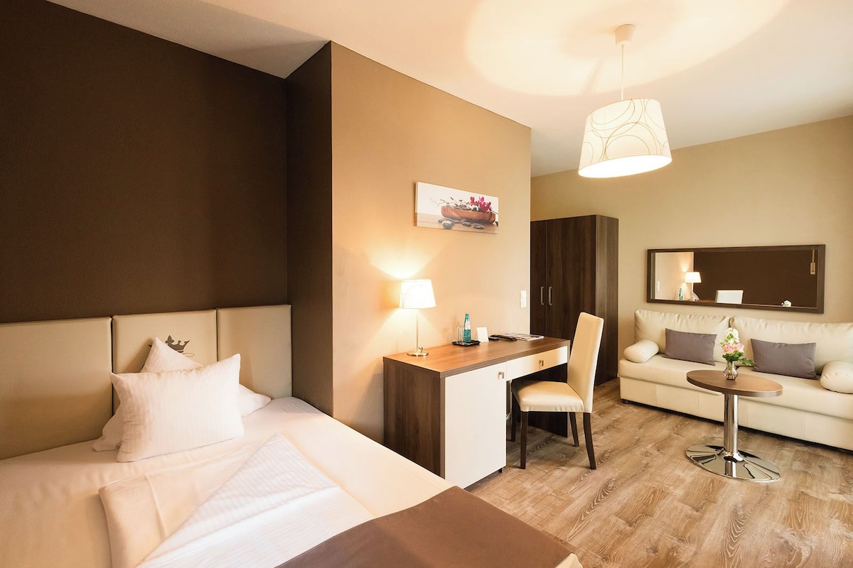 A hotel room with a bed, desk, chair, and sofa.