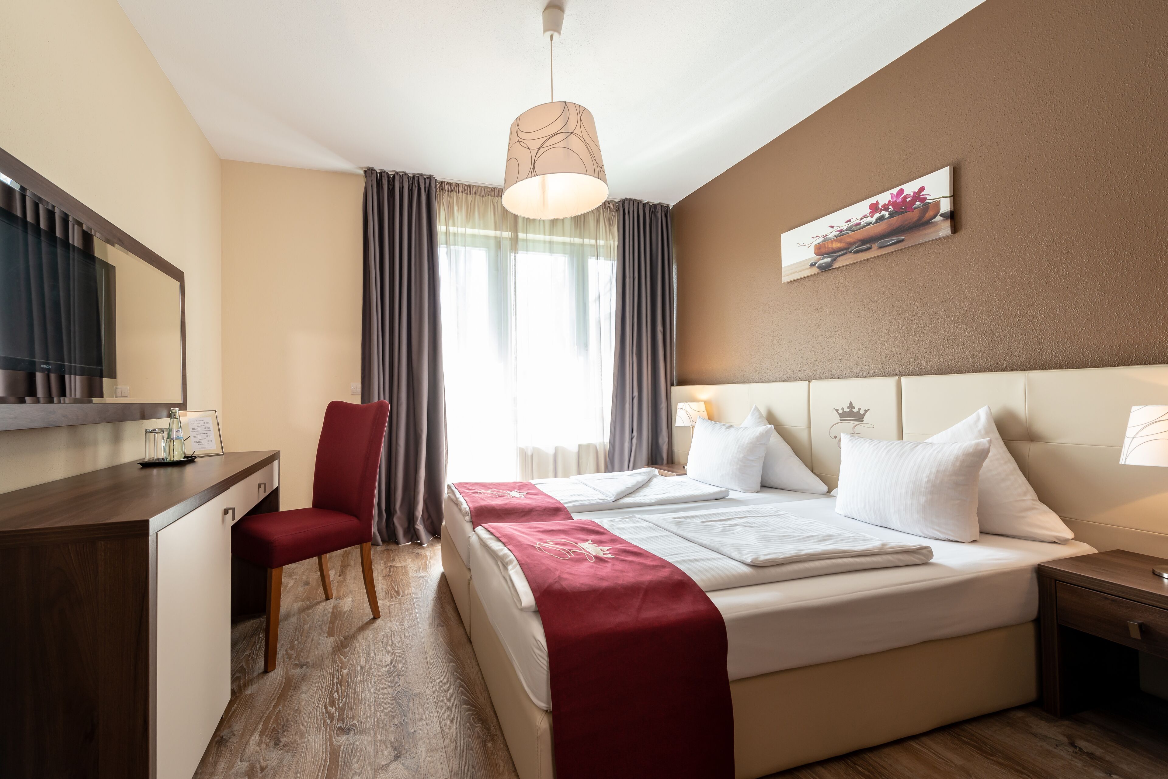 A hotel room with a bed, a desk, a chair, a mirror, and a painting on the wall.