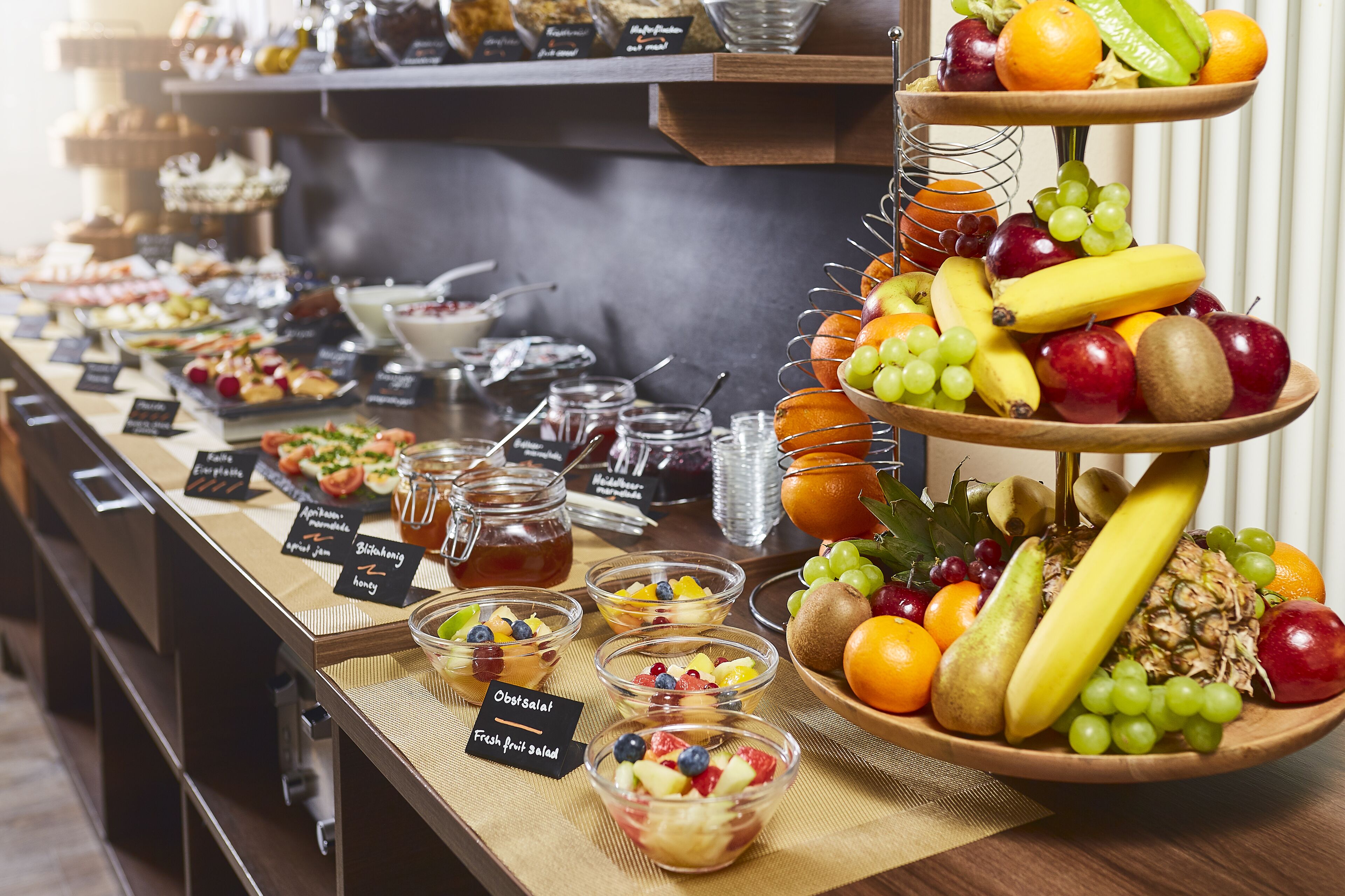 Un bufé con diversas frutas, un frutero y un letrero que indica ensalada de frutas frescas.