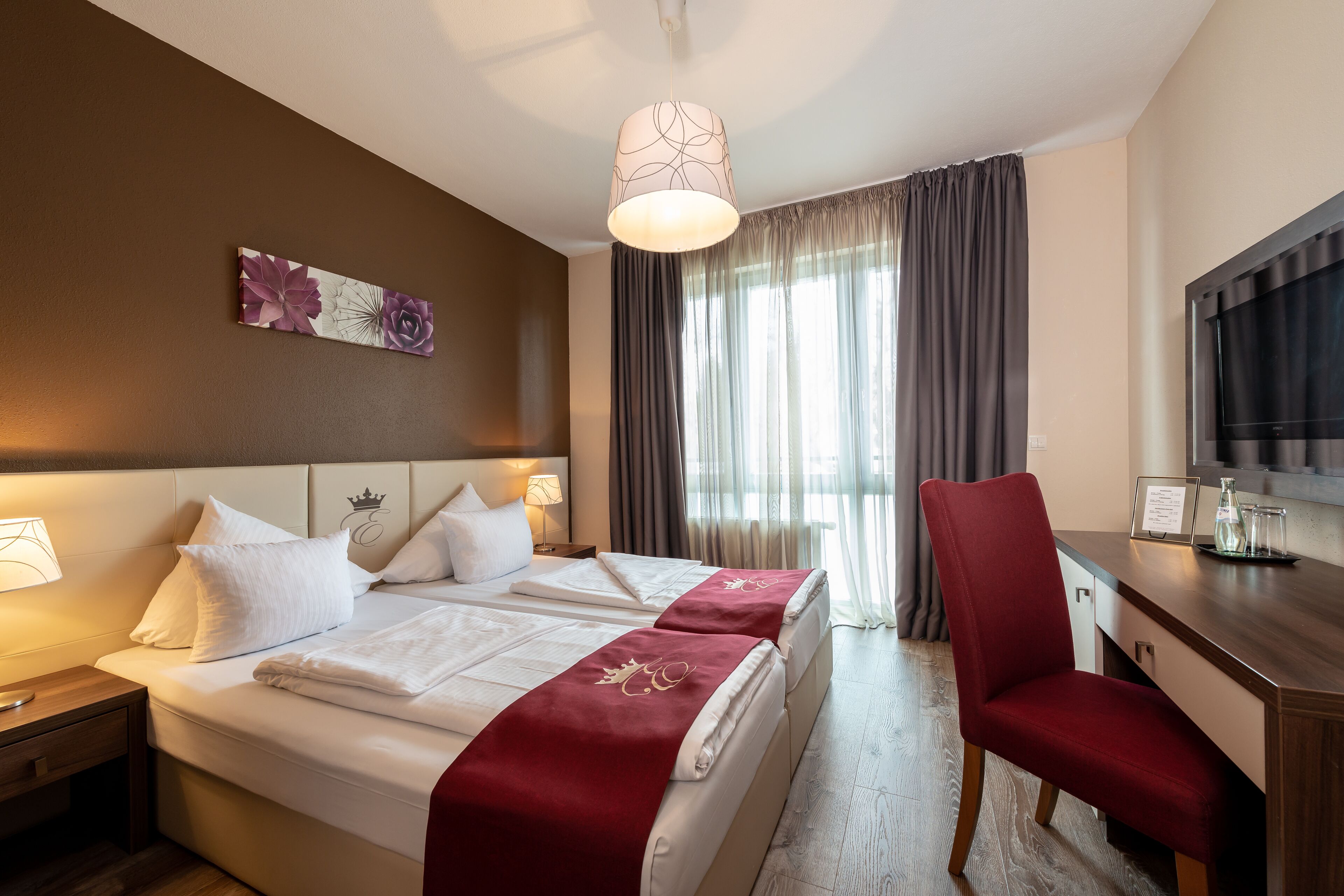 Ein Hotelzimmer mit einem großen Bett, einem Schreibtisch, einem Sessel, einem Fernseher und einem Fenster mit Vorhängen.