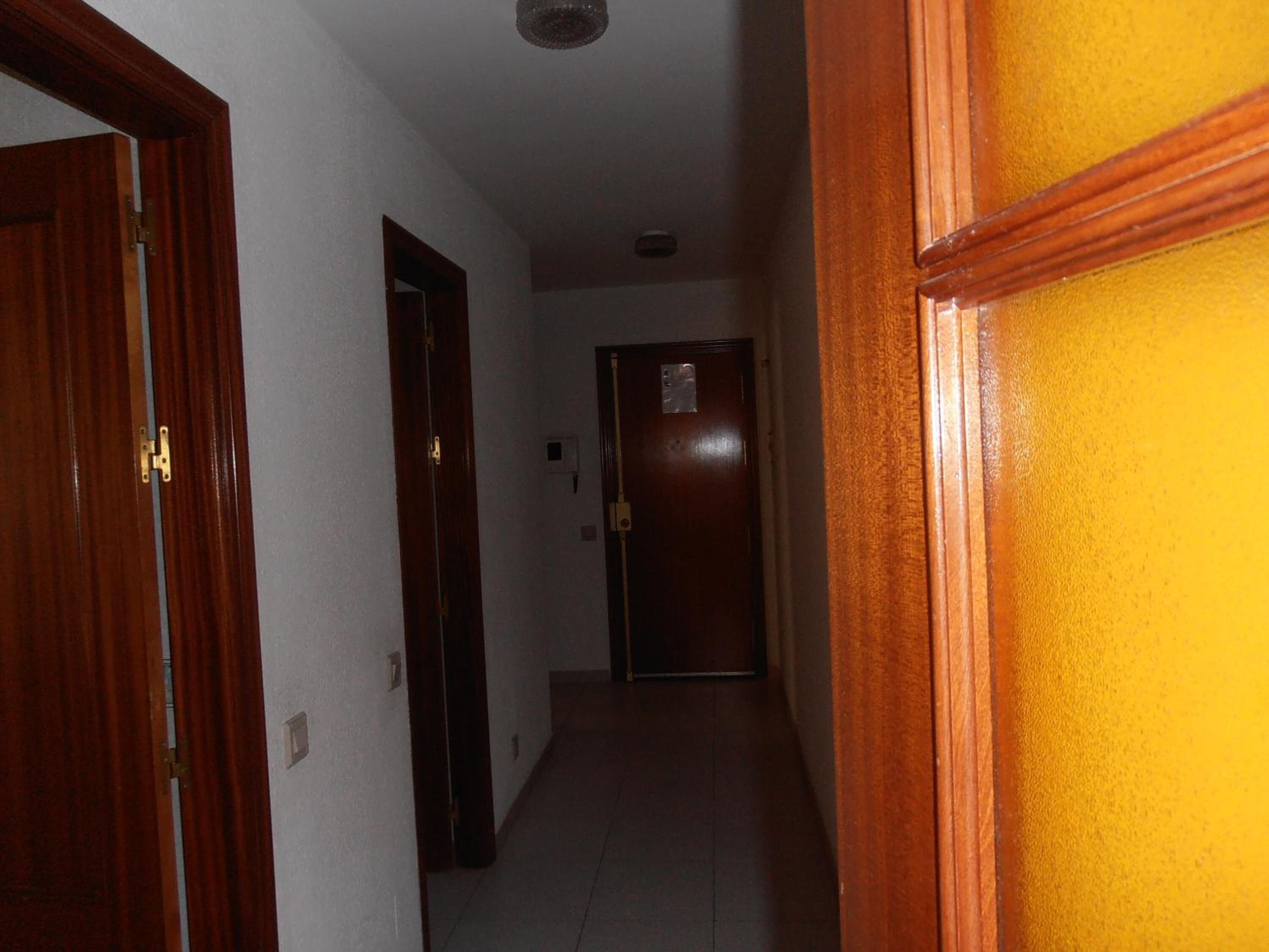 A narrow hallway with wooden doors and a plain white wall.