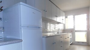 Eine Küche mit weißen Schränken, einem Kühlschrank, einer Spüle und einem Fenster mit Vorhängen.