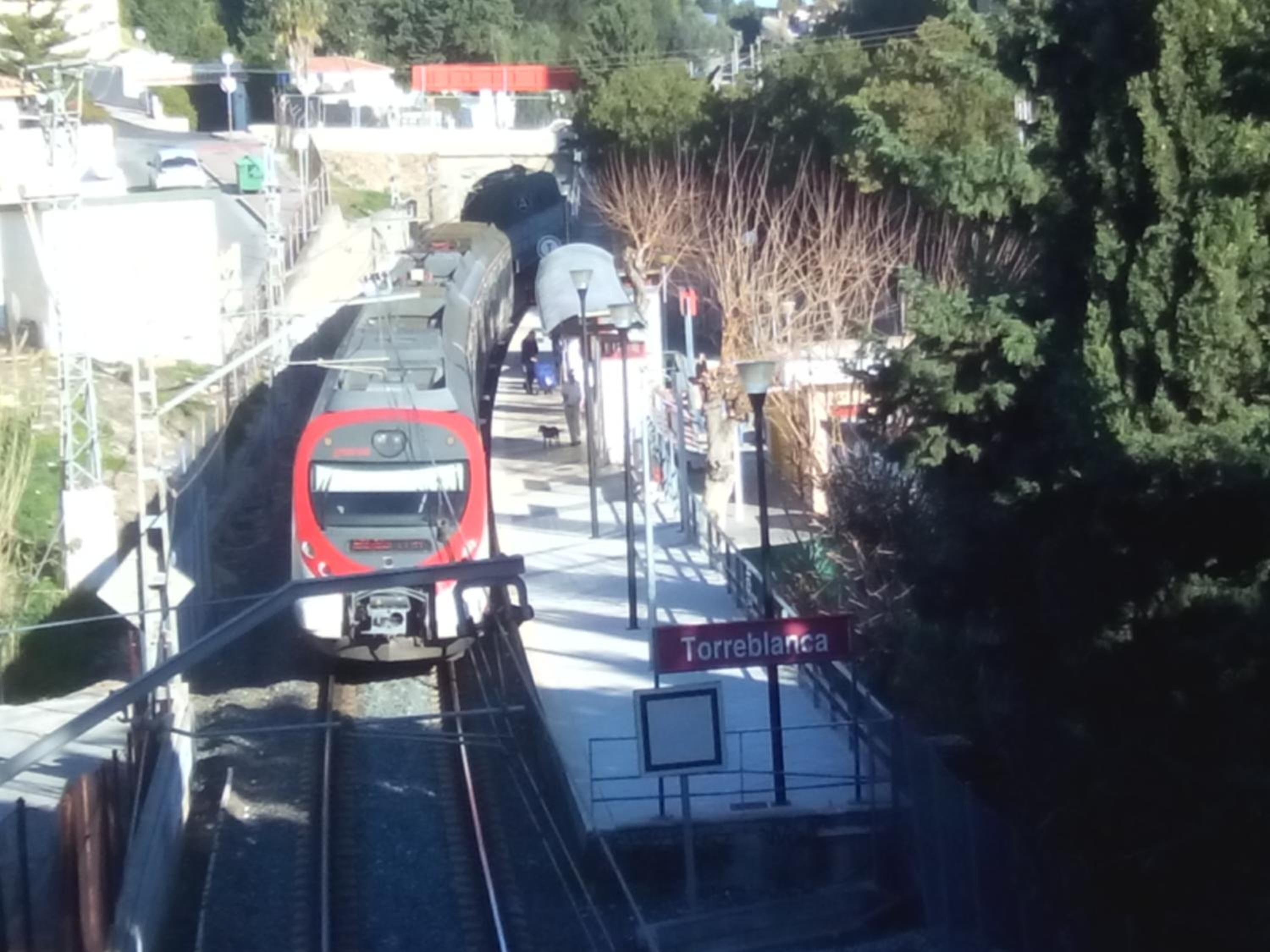 Andén de estación de tren con un tren rojo acercándose.