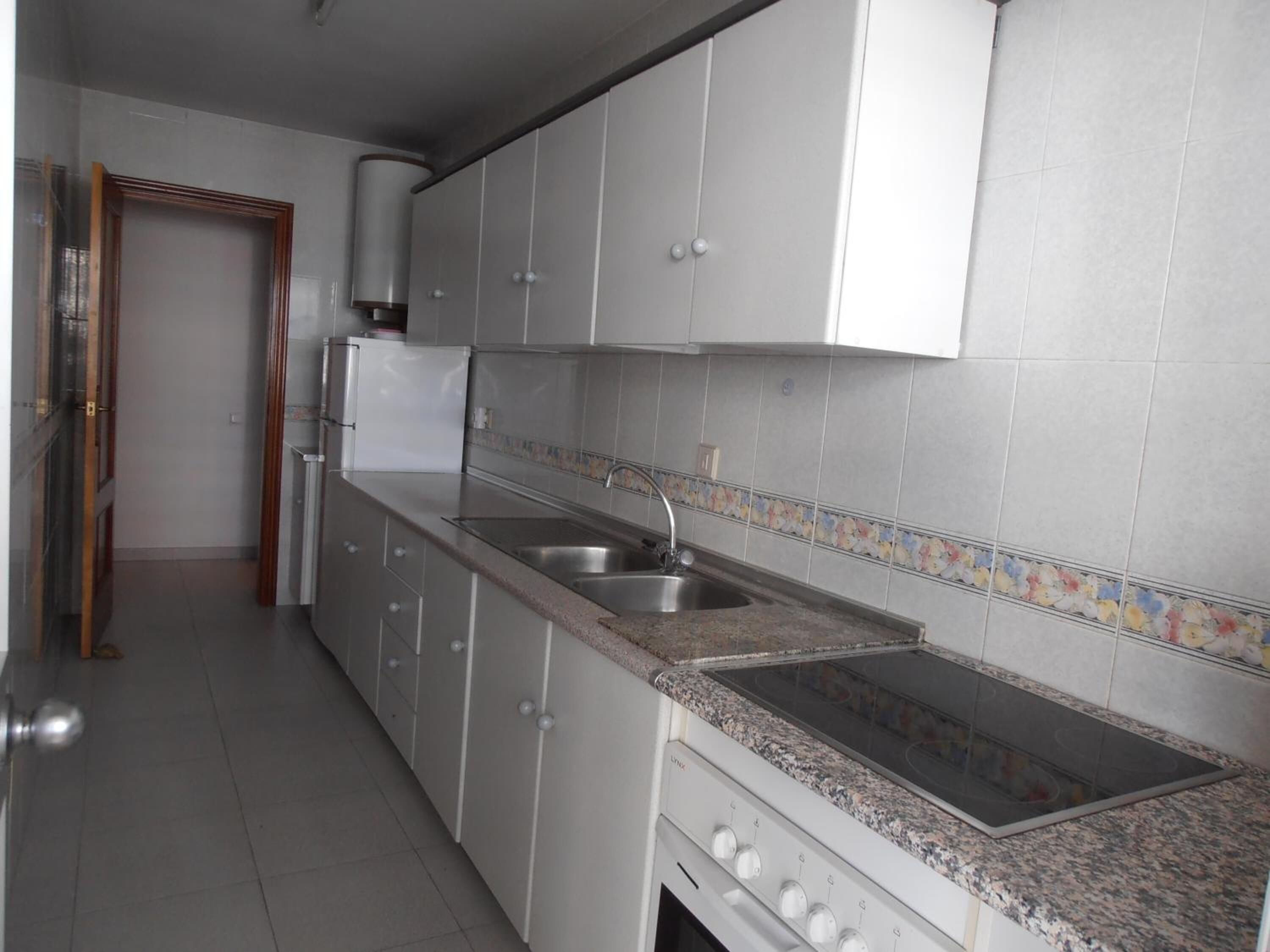 Una cocina con armarios blancos, encimera de granito, pileta de acero inoxidable y horno empotrado.