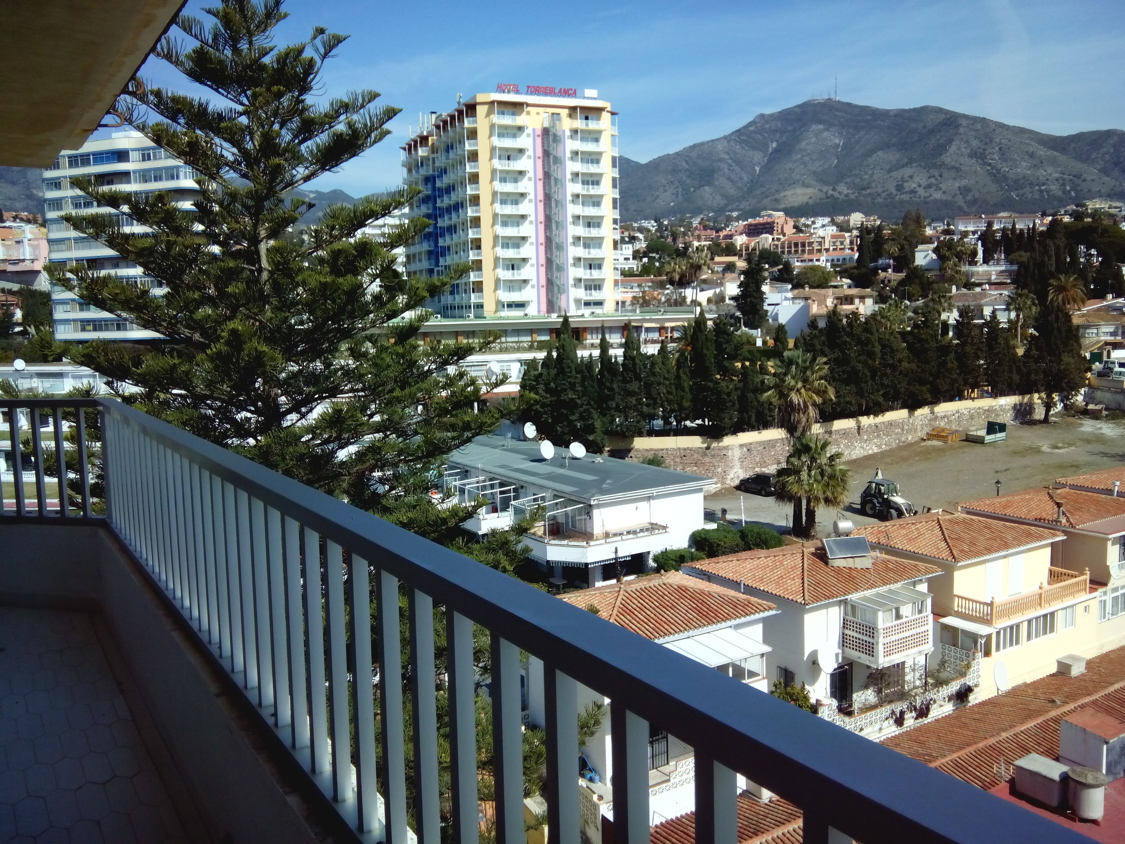 A hotel with multiple floors, a balcony, and a view of the surrounding town and mountains.