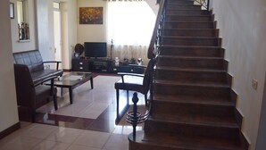 Sala de estar com sofá, mesa de centro e rack para TV. Escada com corrimão leva a outro andar.