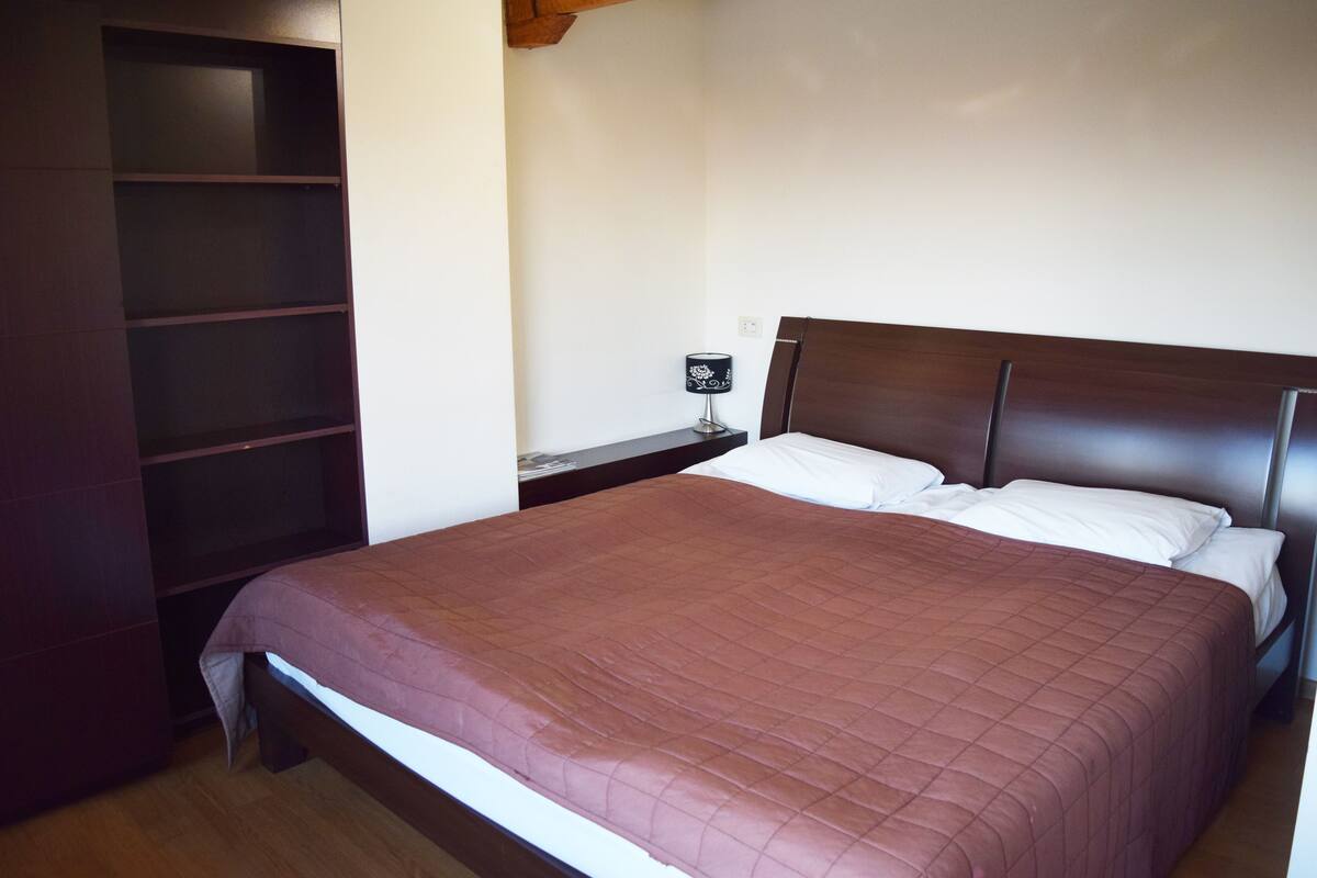 Un dormitorio con una cama grande, cabecera de madera, mesita de noche y estantería empotrada.