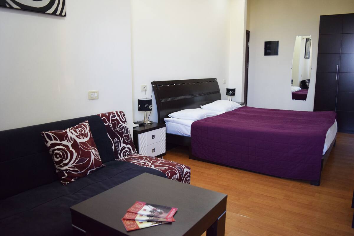 Una habitación de hotel con cama, sofá, mesita de noche, mesa y espejo.
