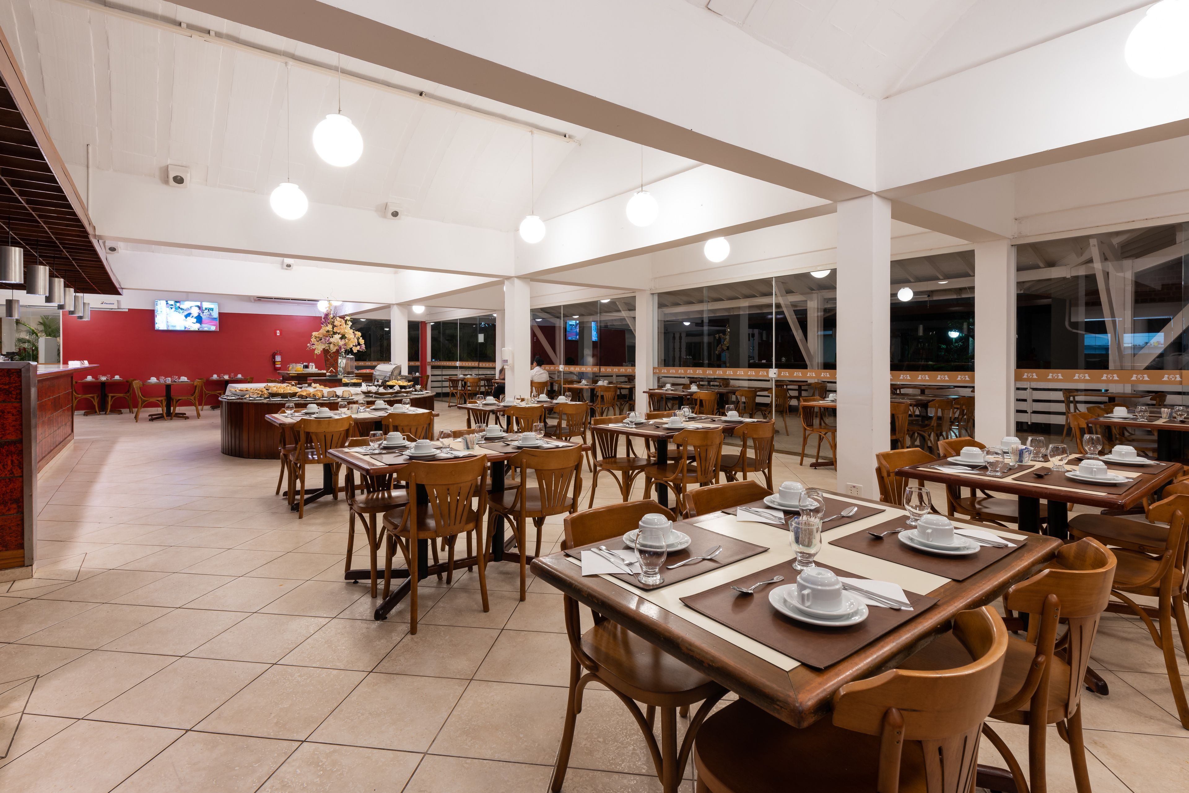 Un restaurante espacioso con varias mesas y sillas, ventanas amplias y lámparas colgantes.