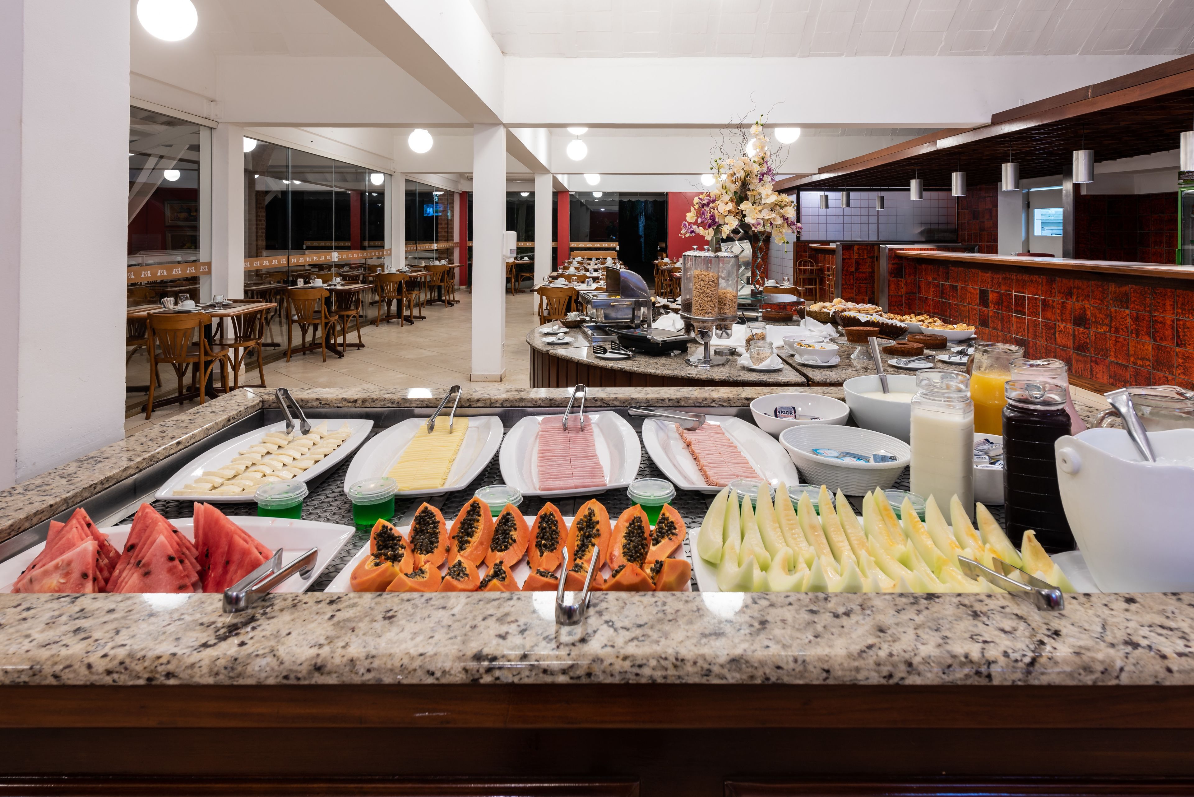 A buffet with various food items and a seating area in the background.