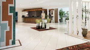 Un vestíbulo amplio con un mostrador de recepción, un gran jarrón decorativo y plantas en macetas.