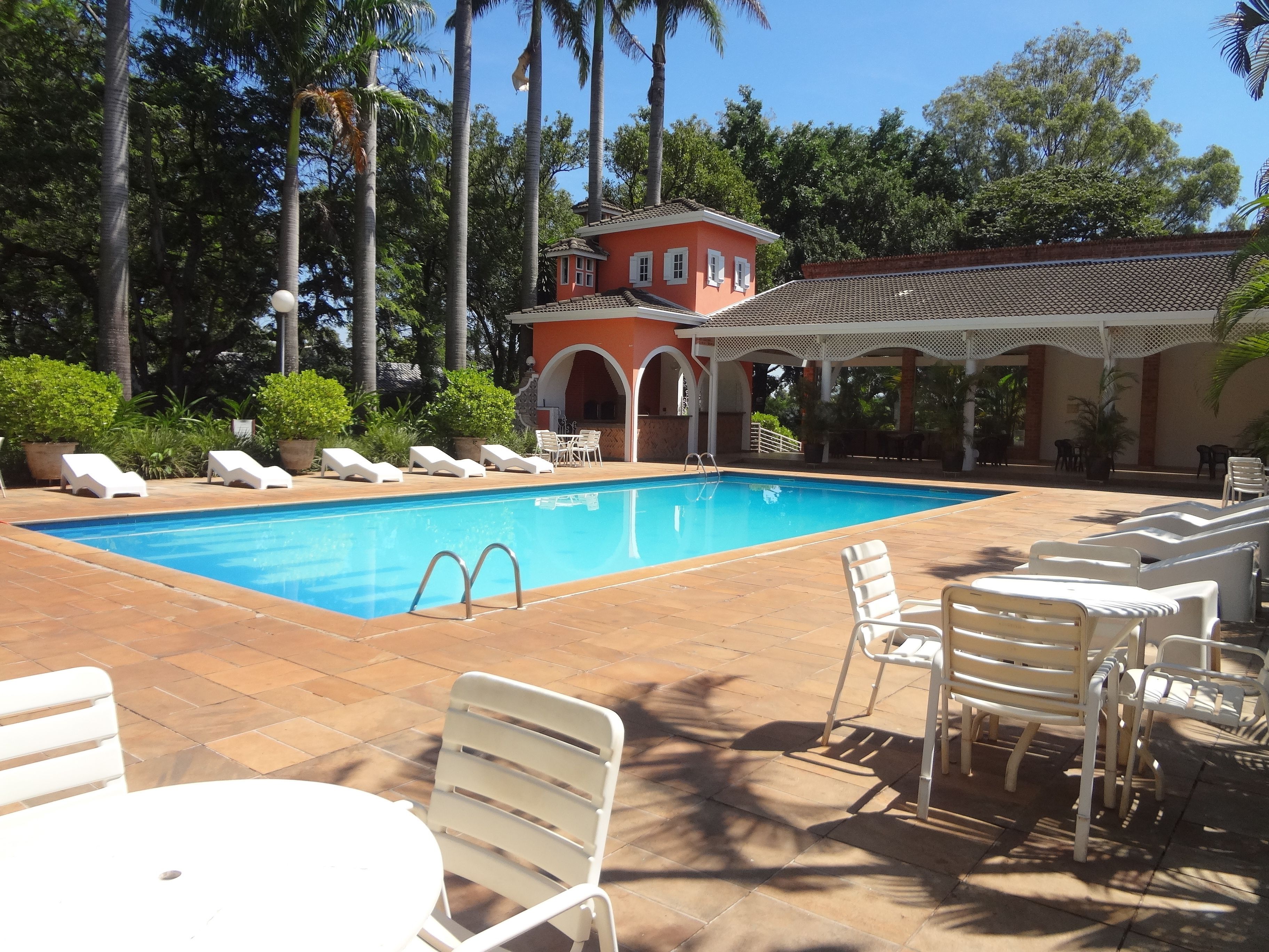 Ein Pool mit Liegestühlen und Tischen, umgeben von Palmen und einem Gebäude mit einem Ziegeldach.