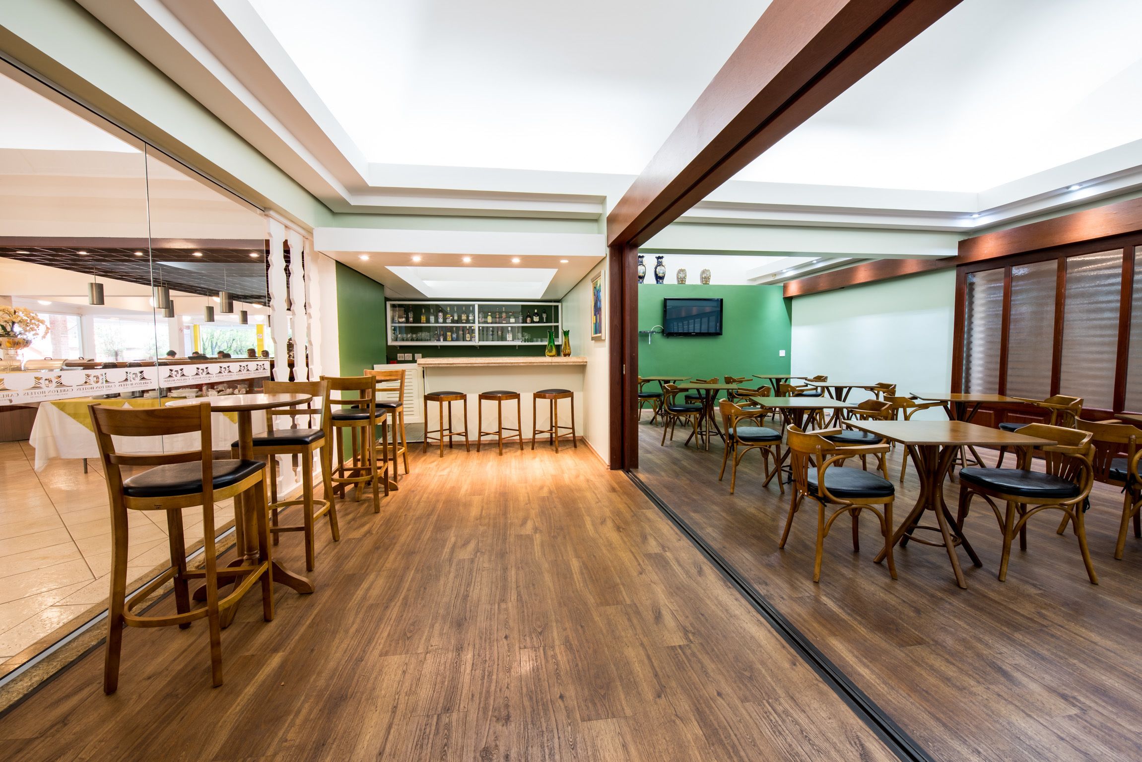 Un amplio comedor con mesas y sillas de madera, una zona de bar con estantes y una pared verde de acento.