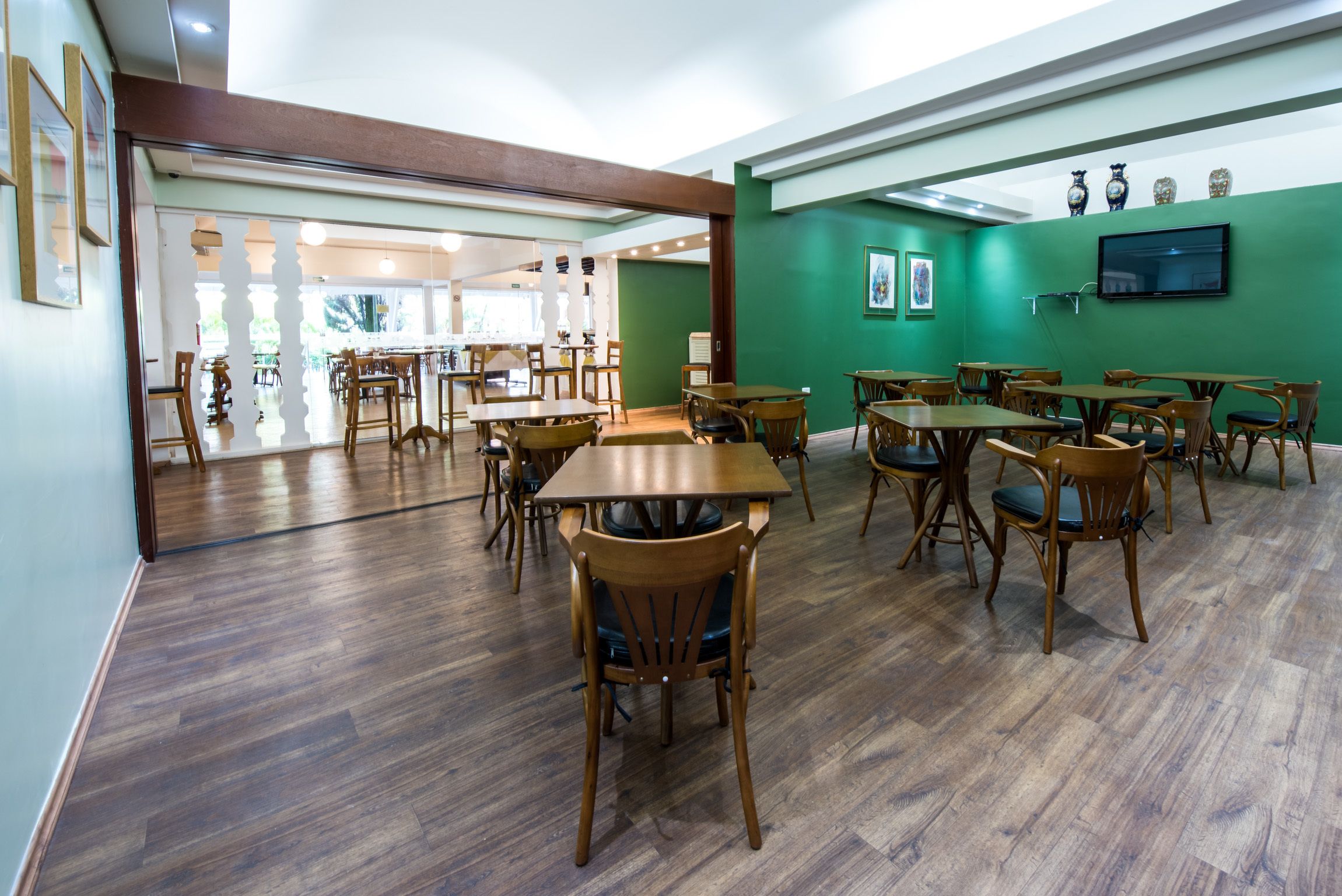 A spacious dining area with wooden tables and chairs, a green accent wall, and a flat-screen TV mounted on the wall.