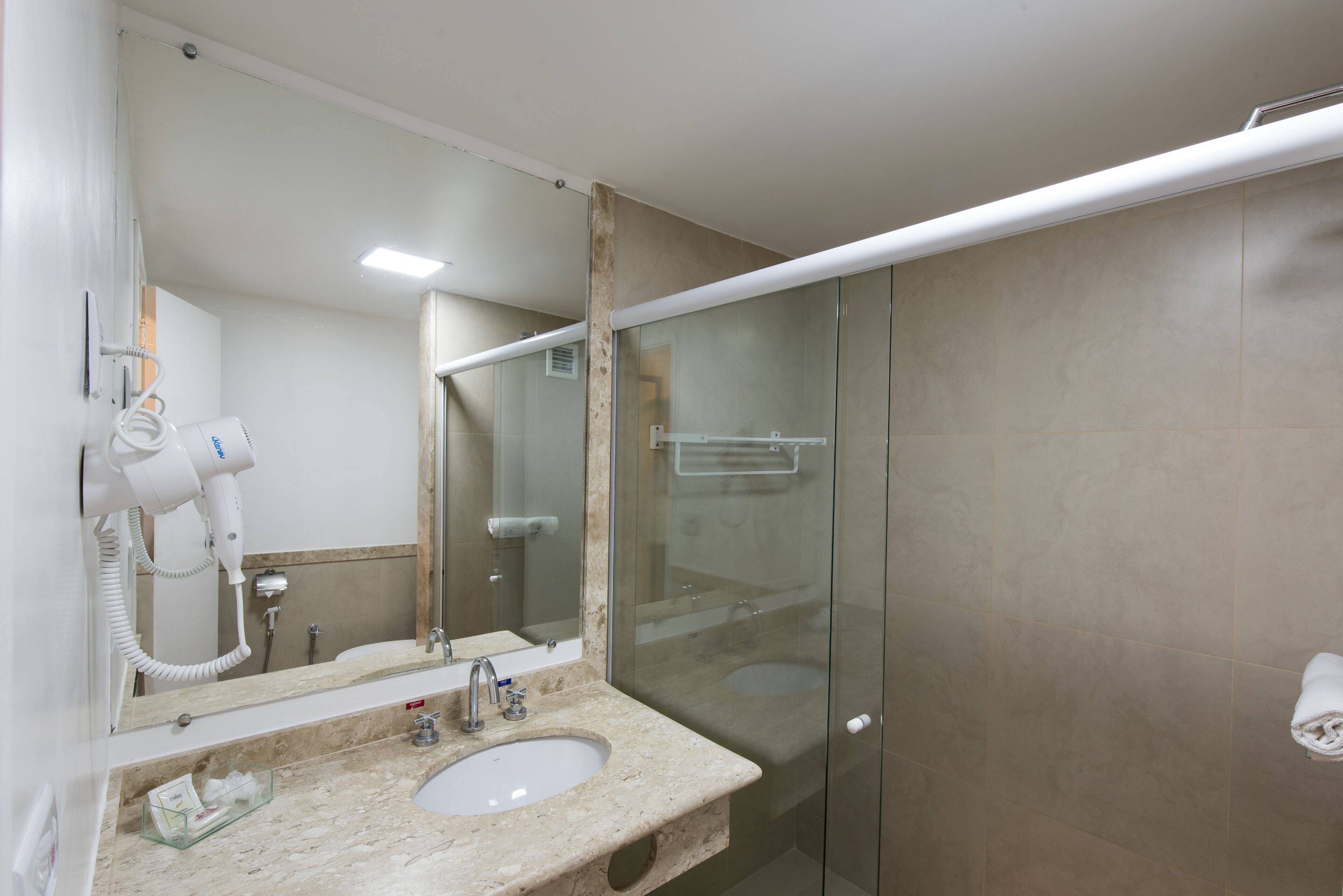 Un baño con lavamanos, espejo, secador de pelo y cabina de ducha de vidrio.