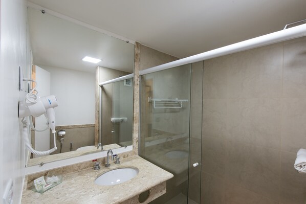 A bathroom with a sink, mirror, hairdryer, and glass shower enclosure.