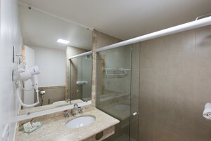 Un baño con lavamanos, espejo, secador de pelo y cabina de ducha de vidrio.
