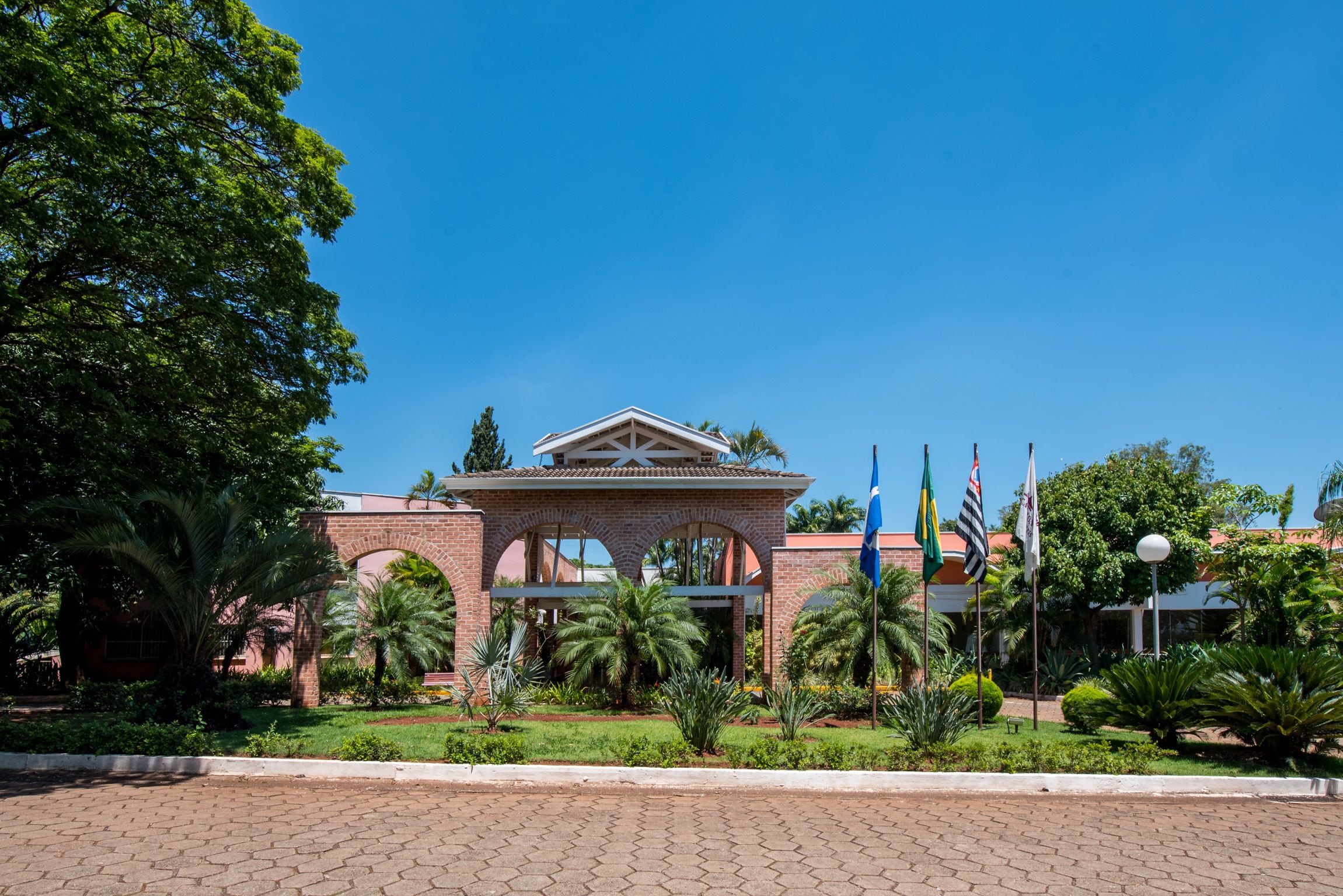 A building with a central archway, surrounded by greenery and palm trees.