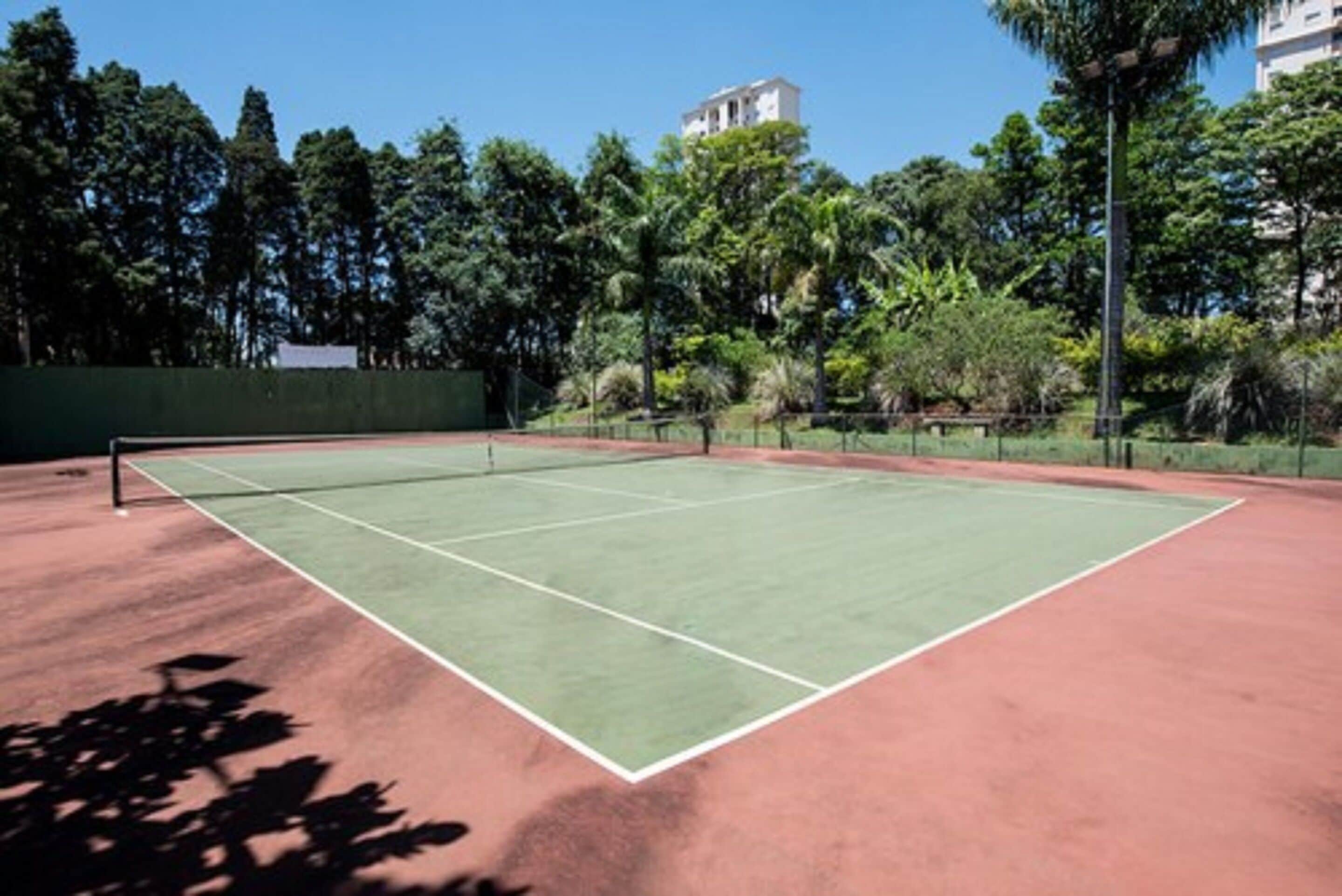 A tennis court with a net, surrounded by trees and a building in the background.