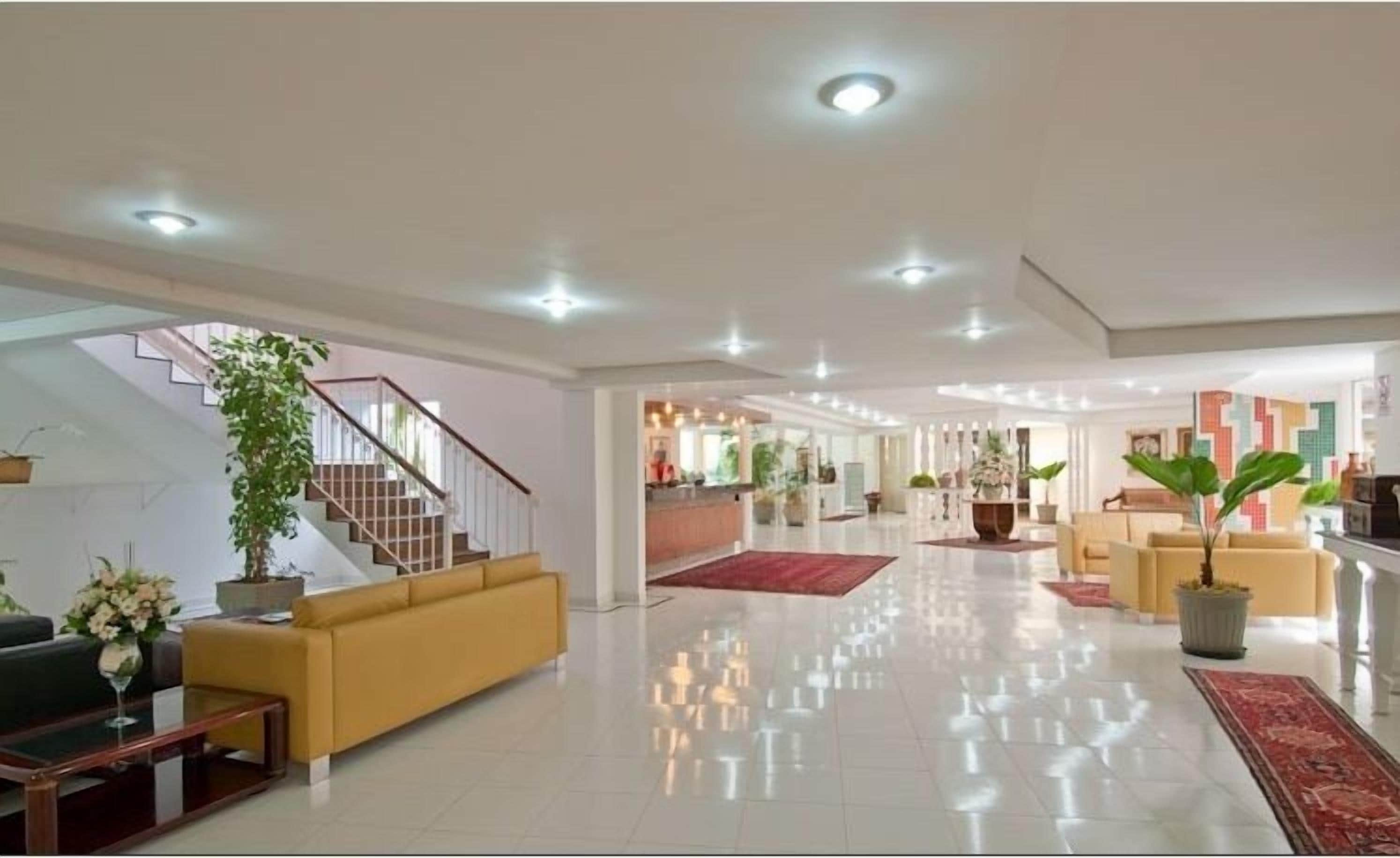 A spacious lobby with a staircase, a reception desk, and several seating areas.