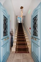 Una escalera con alfombra estampada, puertas azul claro con herrajes negros y un jarrón con flores a la izquierda.