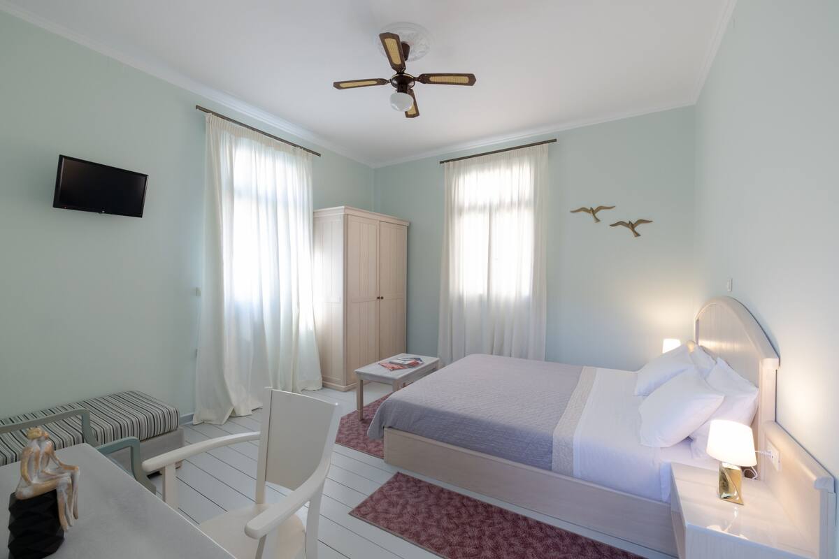 Una habitación de hotel con cama, escritorio, silla, televisor y ventilador de techo.