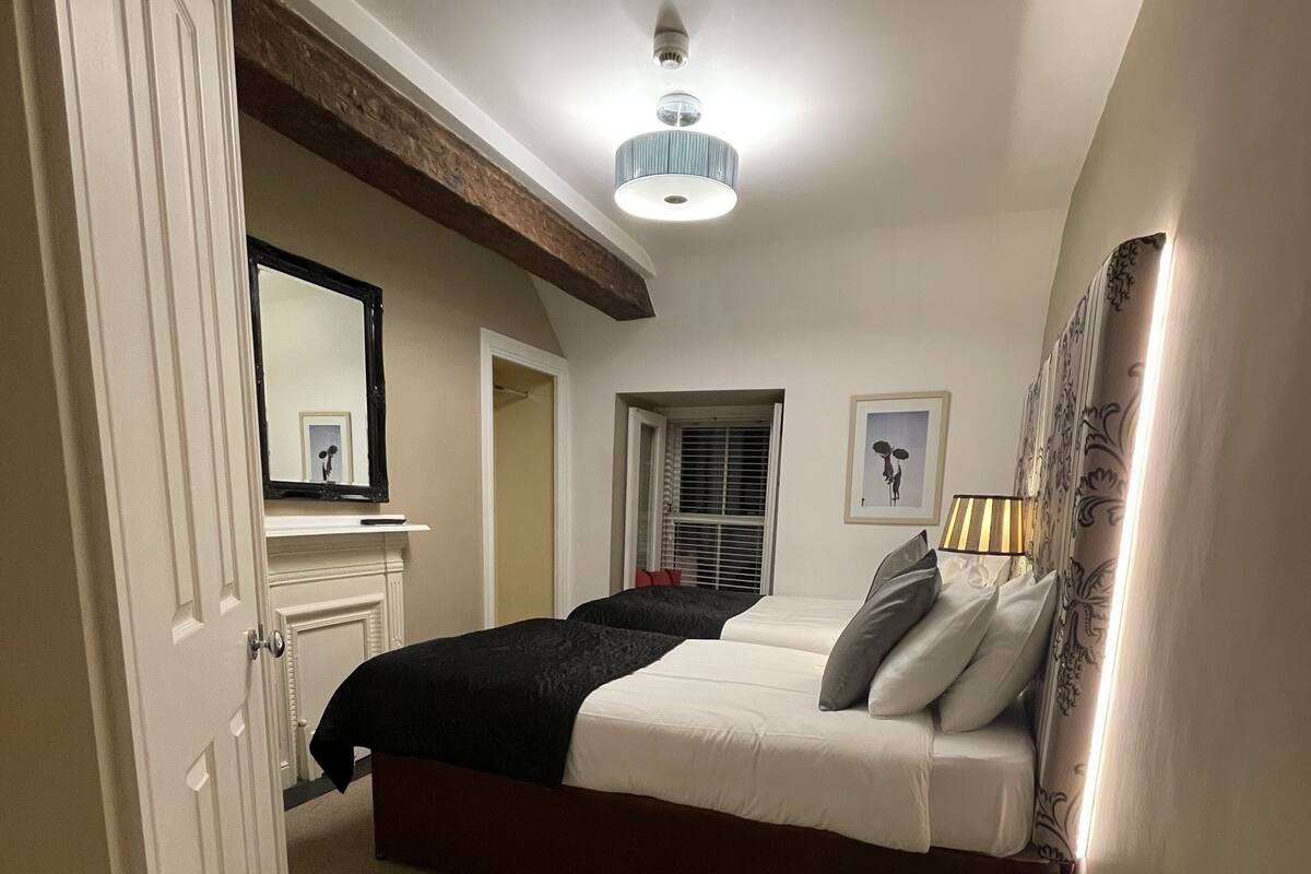 A bedroom with a bed, a bedside lamp, a window with blinds, a door, and a ceiling light.