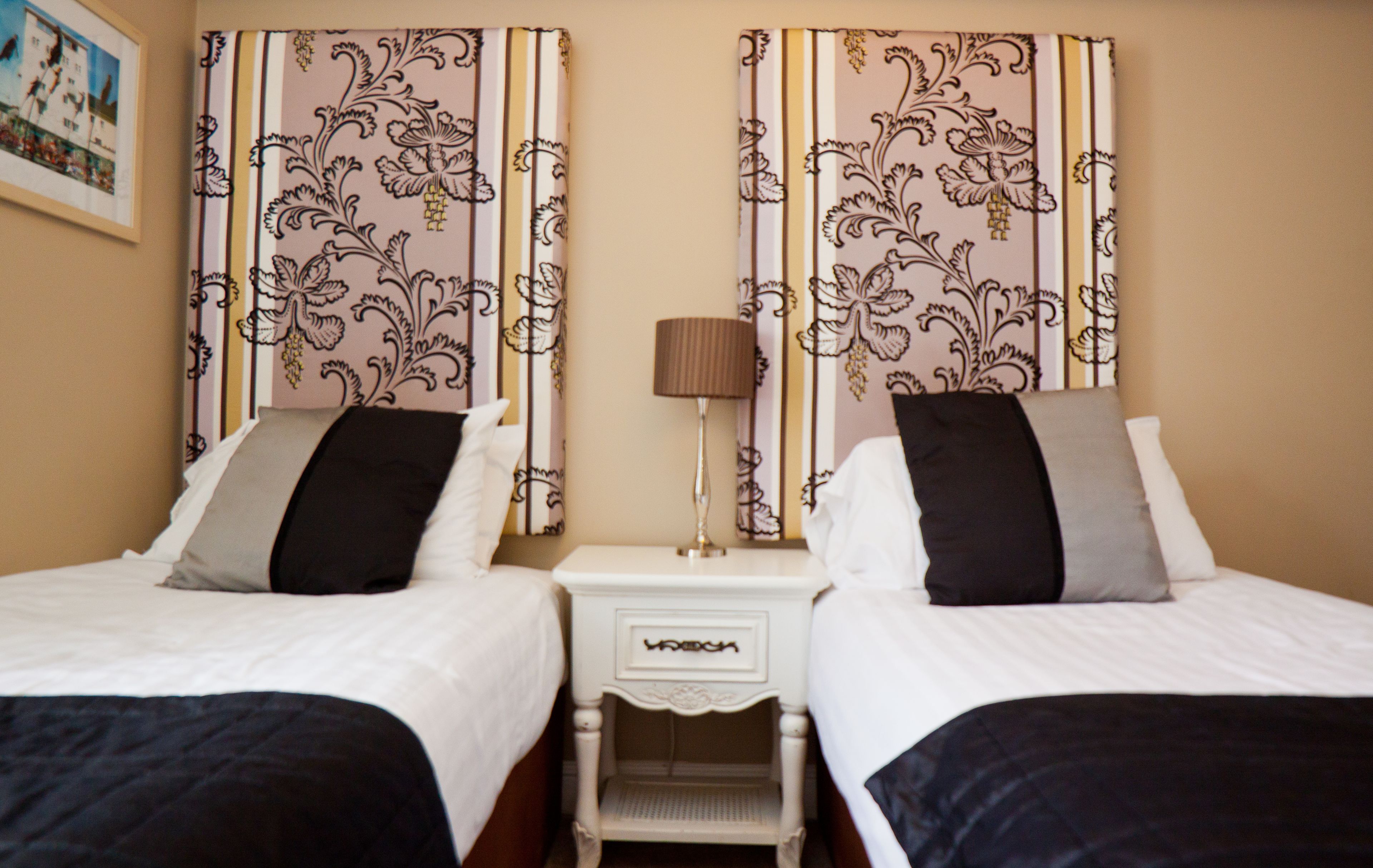 A hotel room with two single beds, a nightstand between them, and a lamp on the nightstand.