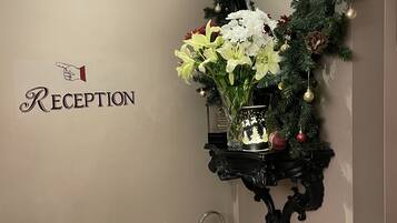 Un área de recepción con un cartel, un adorno navideño, un arreglo floral y un farol.