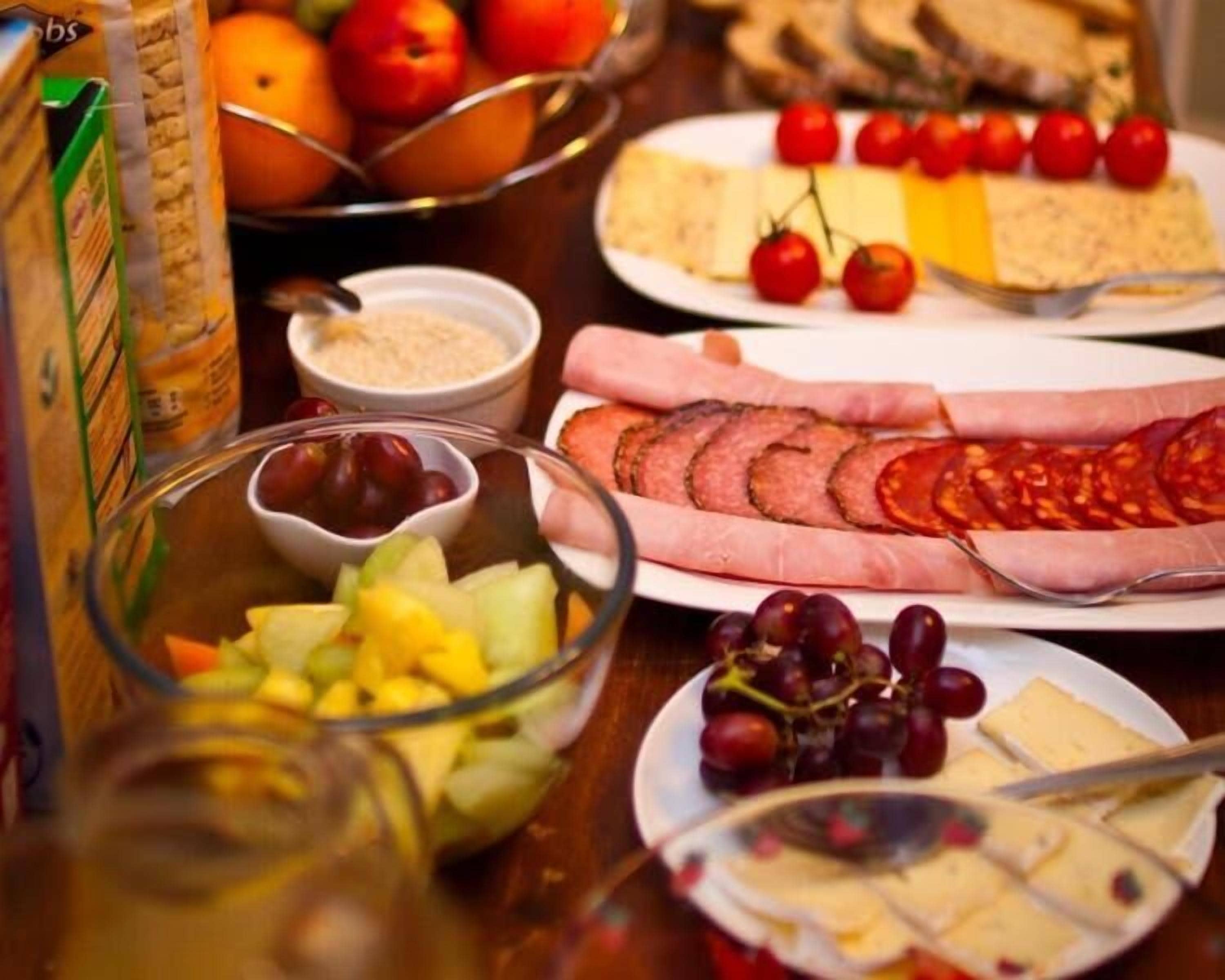 Une table sur laquelle on trouve divers aliments, notamment des tranches de jambon, du fromage, des raisins et un saladier de fruits.