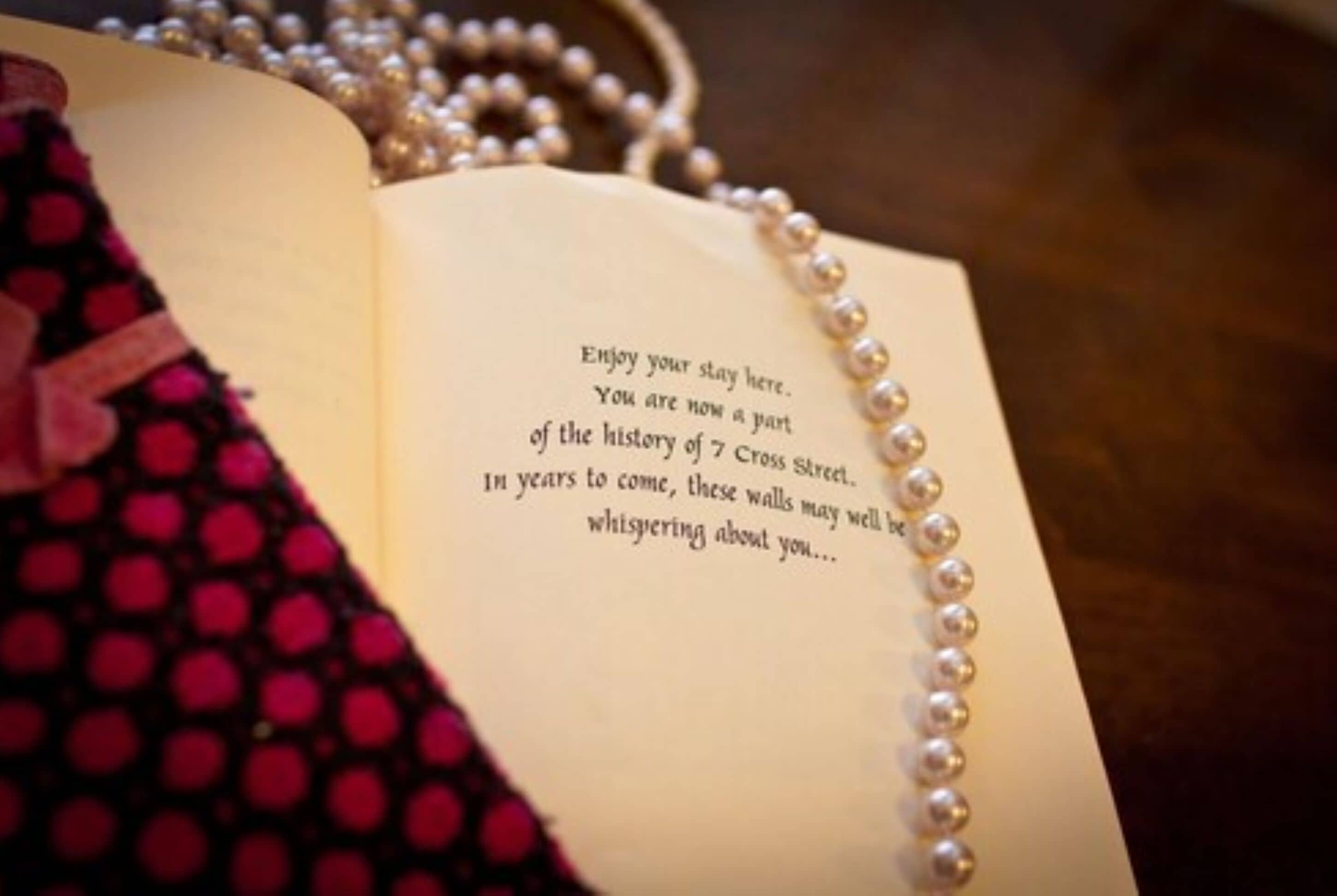 An open book with a message on its page, surrounded by a string of pearls.