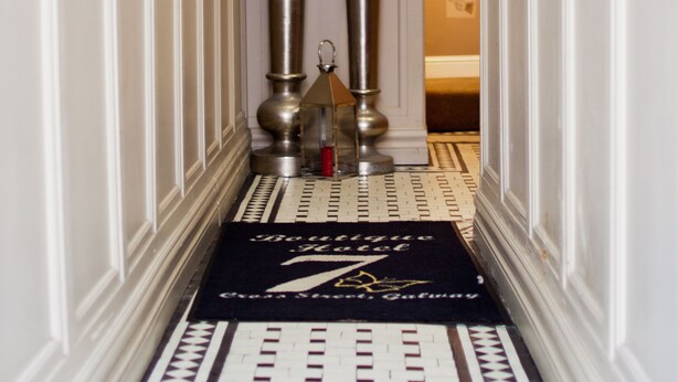 A hallway with a black and white patterned floor, two tall metallic columns with greenery on top, and a reception area with a sign displaying the number 7. - 7 Cross Street (Galway)