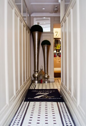A hallway with a black and white patterned floor, two tall metallic columns with greenery on top, and a reception area with a sign displaying the number 7. - 7 Cross Street (Galway)
