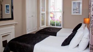 A bedroom with two beds, a fireplace, a window with blinds, and a framed picture on the wall. - 7 Cross Street (Galway)