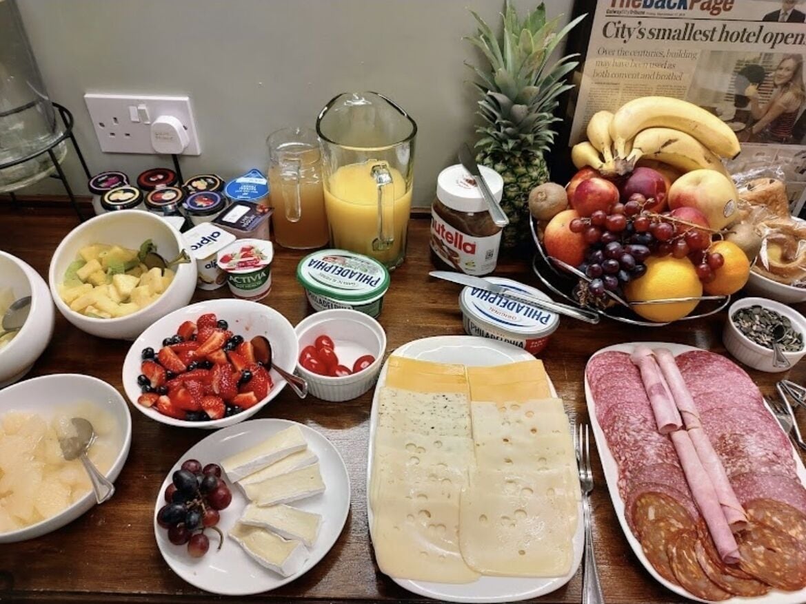Una mesa de desayuno con diferentes alimentos, como frutas, quesos y embutidos.
