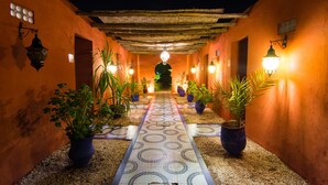A corridor with patterned floor tiles, potted plants, and wall-mounted lights. - Le Relais De Marrakech (Marrakech)