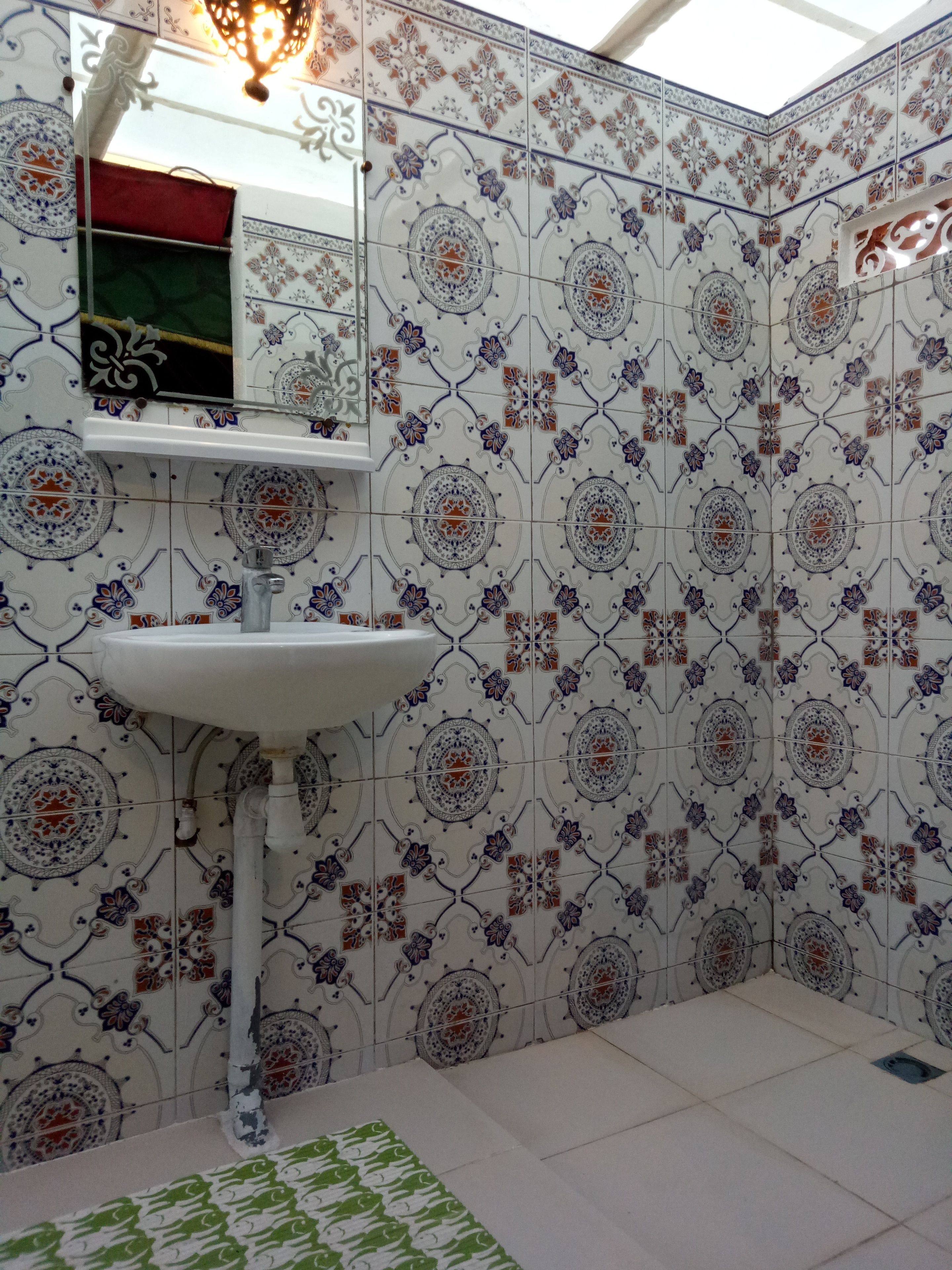 Um banheiro com pia branca assentada em pedestal, padrões de azulejos decorativos nas paredes e um tapete de padrão verde no chão.